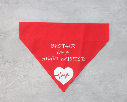 A red triangular bandana with the text 'BROTHER OF A HEART WARRIOR' printed in white. Below the text, there is a white heart graphic with a red heartbeat line running through it. The bandana is laid flat on a gray surface.