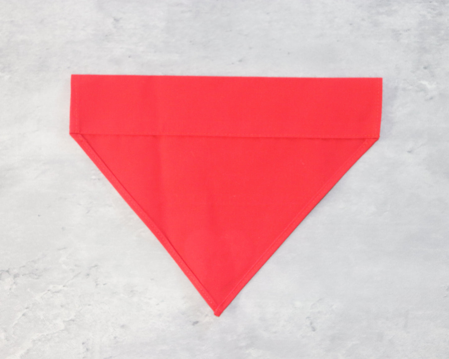 A red triangular bandana The bandana is laid flat on a gray surface.