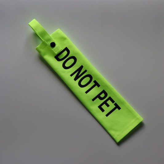 A fluorescent yellow fabric lead sleeve with a black button snap. The sleeve features bold black text that reads 'DO NOT PET.' Designed for dog handlers who need to signal that their dog should not be approached or touched, its bright color and clear typography ensure the message is highly visible. Ideal for service dogs, reactive dogs, or pets needing space, this sleeve helps prevent unwanted interactions while keeping the dog's focus on their handler.