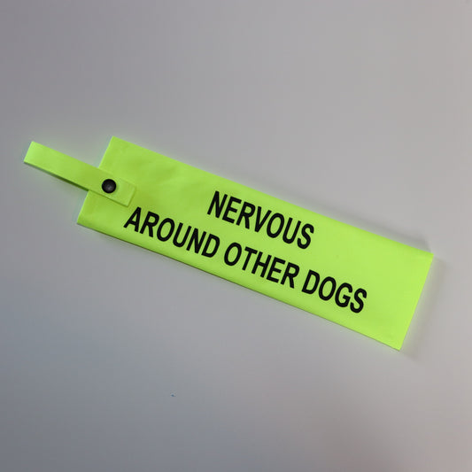 A fluorescent yellow fabric lead sleeve with a black button snap. The sleeve features bold black text that reads 'NERVOUS AROUND OTHER DOGS.' Designed to help dog owners communicate that their pet may feel anxious or uncomfortable in social settings, this sleeve increases awareness and helps prevent stressful interactions. Ideal for nervous dogs needing space, the high-visibility design ensures the message is clear.
